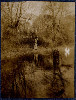 Photograph of a woman with bird by a wooded lake