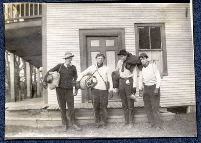 Photograph of four men with packs in front of a house