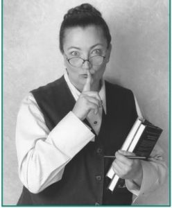 Black and white photograph of a woman librarian making the "Shh" symbol.