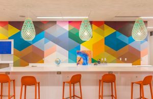 This shows a bar style set up of a long table and high bar stool like chairs against a colorful wall. It's an example of what a library room might look like.